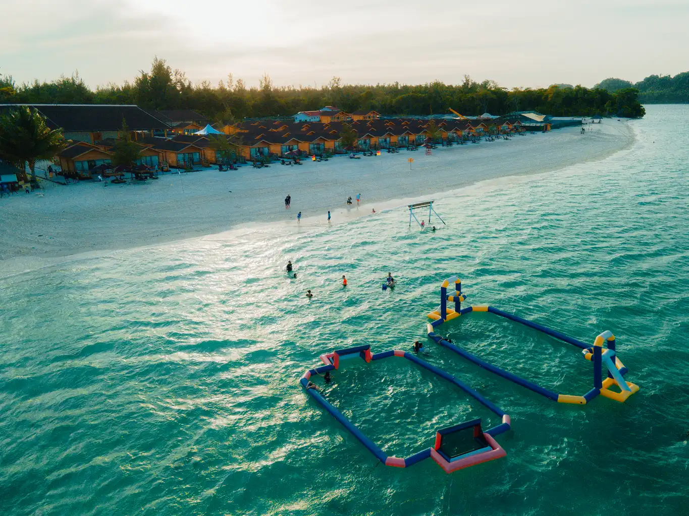 Aerial view of a JSK Mantanani Island Resort beach with a floating water park and beachfront huts.