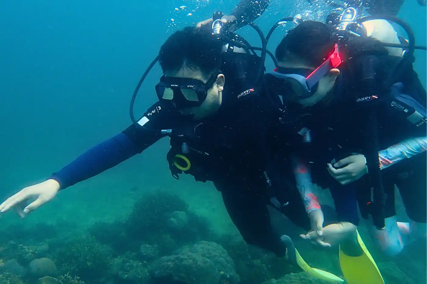 Two scuba divers exploring underwater near Mantanani Island, observing coral reefs.